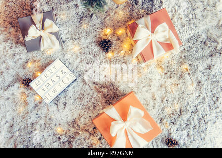 Top view composition of lighted box with Merry Christmas and New year wishes and presents in colorful festive wrapping tied with bow under xsmas tree  Stock Photo