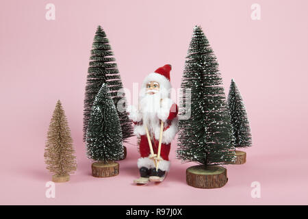 a Santa Claus figurine skiing among miniature firs on a pink background. Color harmony. Minimal still life color photography Stock Photo