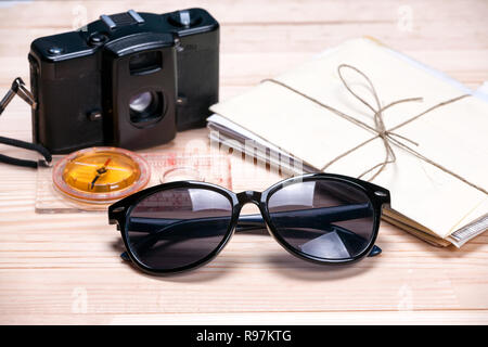 Sunglasses, compass, old film camera and a bunch of letters on light natural wooden background. Concept of summer holidays. Stock Photo
