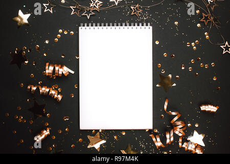 Holiday golden decorations and white notebook on black background. Flat lay style. Planning concept. Stock Photo