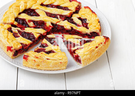Homemade berry pie with cherries and raspberries cut into pieces on white wooden table. Shallow focus. Stock Photo