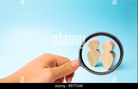 Magnifying glass is looking at the Two people stand together and talk. Two wooden figures of people conduct a conversation on a blue background. Place Stock Photo
