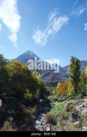 A stream in Imlil Valley in the foothills of the Atlas Mountains - high peaks in the background and a rocky stream surrounded by trees in the foregrou Stock Photo