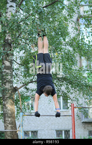 Kovrov, Russia. 11 August 2013. Teen is engaged in discipline gimbarr on a horizontal bar in the courtyard of a multi-storey residential building Stock Photo