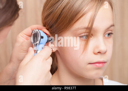 Female pediatrician examines elementary age girl's ear. Doctor using a otoscope or auriscope to check ear canal and eardrum membrane. Child ENT check  Stock Photo
