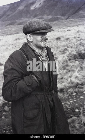 1940s, historical, a Welsh coal miner in coat and flatcap walking by a hillside, in a valley at Merthyr, South Wales, UK. Stock Photo