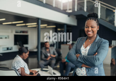 Portrait of a confident black businesswoman smiling with her arms crossed and all african team in the background Stock Photo