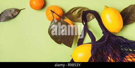 Set of citrus in mesh textile bag on green background. Stock Photo