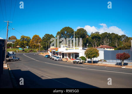 View of the road through Dorrigo with no traffic, vehicles parked in front of buildings and gum trees in the background on an autumn day Stock Photo