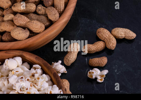 Peanuts with Popcorn in golden wood bowl on black marble table Stock Photo