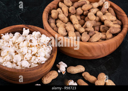 Peanuts with Popcorn in golden wood bowl on black marble table Stock Photo