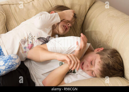 children, boy and girl, brother and sister, siblings, play-fighting, fighting, wrestling, noisy, violent, on sofa, twelve years old, six years old. Stock Photo