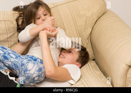 children, boy and girl, brother and sister, siblings, play-fighting, fighting, wrestling, noisy, violent, on sofa, twelve years old, six years old. Stock Photo