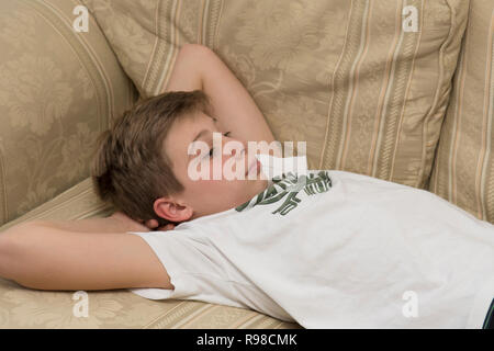 lethargic bored sullen moody lazy twelve-year-old boy laying on a sofa Stock Photo