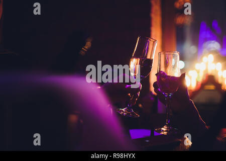 Christmas illuminations and champagne glasses. Hands of people with glasses of champagne, celebrating and toasting in honor of the Christmas and Happy New Year. Couple cheering with champagne flutes. Stock Photo