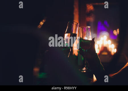 Christmas illuminations and champagne glasses. Hands of people with glasses of champagne, celebrating and toasting in honor of the Christmas and Happy New Year. Couple cheering with champagne flutes. Stock Photo