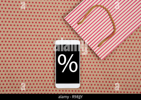 Sale concept - shopping bag and white smartphone with discounts sign on kraft paper background in red polka dots Stock Photo