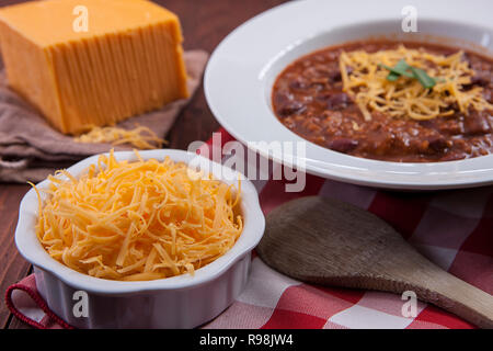 A close up of a small bowl of cheddar heese and a bowl of chili.