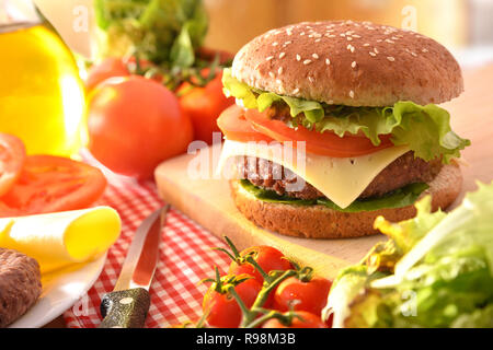 Homemade beef burger with ingredients on table with checkered tablecloth in kitchen. Front view. Horizontal composition. Stock Photo