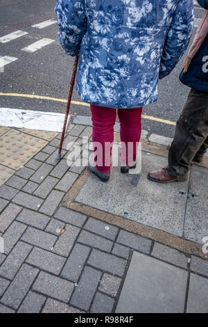 lower body only of Eccentrically dressed elderly man and woman with the aid of a cane waiting to crossing a road in London Stock Photo