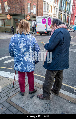 Eccentrically dressed elderly man and woman walking with the aid of a cane discuss crossing a road in London Stock Photo