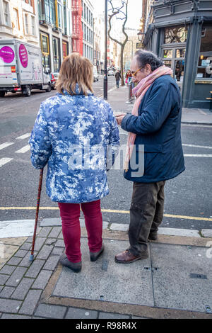 Eccentrically dressed elderly man and woman walking with the aid of a cane discuss crossing a road in London Stock Photo