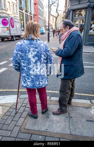 Eccentrically dressed elderly man and woman walking with the aid of a cane discuss crossing a road in London Stock Photo