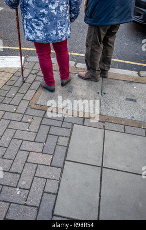 lower body only of Eccentrically dressed elderly man and woman with the aid of a cane waiting to crossing a road in London Stock Photo