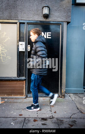 Young man walking past a Black office door with Large letters saying Number One stuck on the door in London, Uk Stock Photo