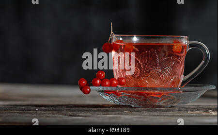 hot viburnum tea in a transparent cup with a handle and saucer on a black background Stock Photo