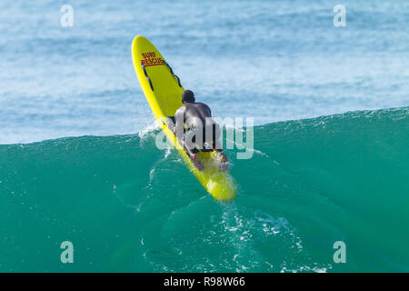 Lifeguard black african man paddling out to ocean backline over wave on yellow surf rescue craft. Stock Photo