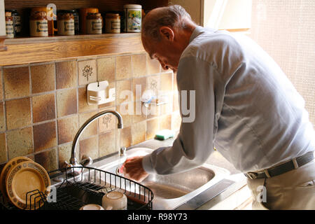 Senior man in kitchen doing dishes by hand at home Stock Photo