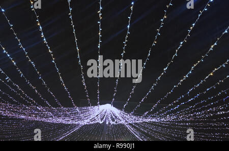 Light bulbs on strings decoration in the snowing sky at night, blue light background Stock Photo