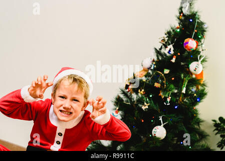 Toddler boy with funny face wearing Santa costume trying to scare like the grinch, expressions and christmas concepts on isolated white background. Stock Photo