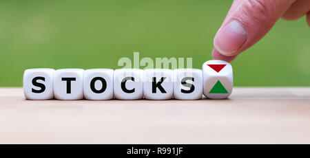 Hand is turning a dice and changes the direction of an arrow symbolizing that the stock market is going up (or vice versa) Stock Photo