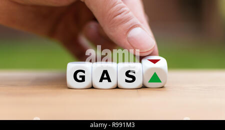 Hand is turning a dice and changes the direction of an arrow symbolizing that the price for gas is changing the trend and goes up instead of down (or Stock Photo