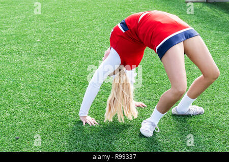 A high school cheerleader is in a bridge while warming up doing a back walk over on green turf. Stock Photo