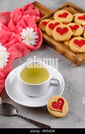 White cup of green tea and cookies with hearts on a gray background. Beautiful still life, the mood of Valentine's Day. Close-up. Stock Photo