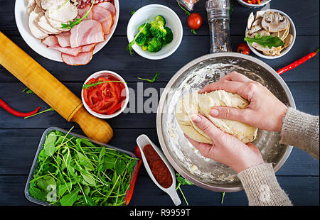 Italian pizza. Hands working with dough preparation pizza or pie making ingredients on table. Dough, cheese, tomatoes, broccoli, mushrooms, salami, ha Stock Photo