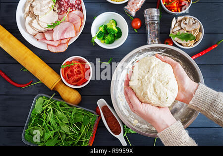 Italian pizza. Hands working with dough preparation pizza or pie making ingredients on table. Dough, cheese, tomatoes, broccoli, mushrooms, salami, ha Stock Photo