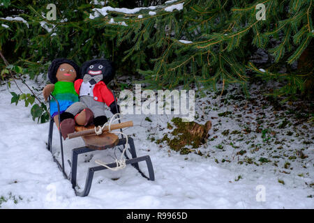 golliwog and brown doll soft toys sitting on small sledge in the snow with christmas trees behind zala county hungary Stock Photo