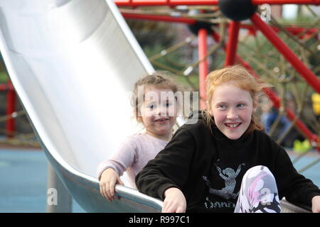 two sisters sliding down a slide on the park in skegness (sunshine park) Stock Photo