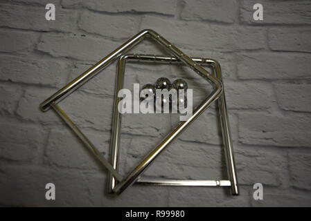 Tangled metal balls between themselves and fishing line with metal stands on the background of a white wall of bricks. Stock Photo