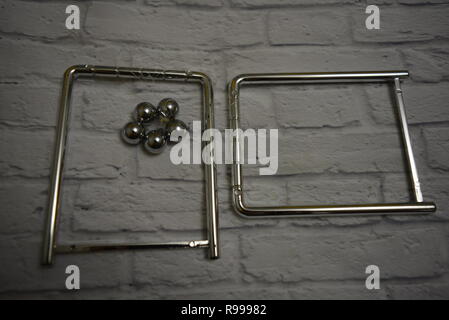 Tangled metal balls between themselves and fishing line with metal stands on the background of a white wall of bricks. Stock Photo