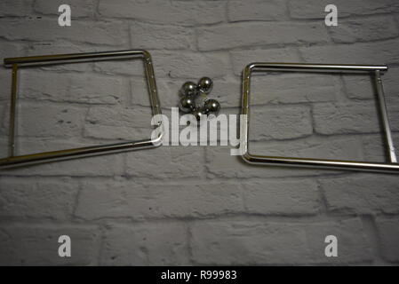 Tangled metal balls between themselves and fishing line with metal stands on the background of a white wall of bricks. Stock Photo
