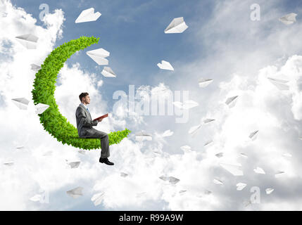 Businessman or student sitting on green moon and reading book Stock Photo