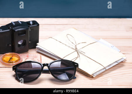 Sunglasses, compass, old film camera and a bunch of letters on a light and blue wooden background. Copy space to the right. Concept of summer time. Stock Photo