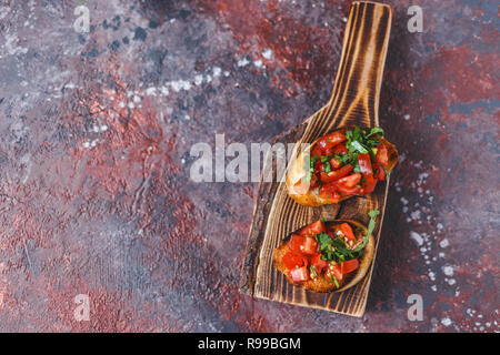 Italian bruschetta with tomatoes and herbs on a wooden board on a dark background Top view Copy space Stock Photo