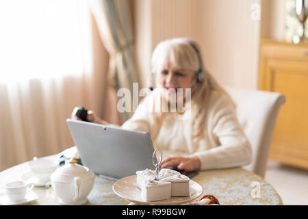 Selective Focus Of A Desert Stand With Cake Standing On The Table. Blurred Image Of Senior Won Playing Games On A Computer At The Background. Stock Photo