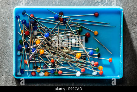Small box with sewing pins. Many multi colored needles. Authentic light. Blades and pricking concept. Fashion industry metaphor. Stock Photo